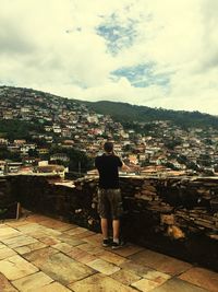 Rear view of man standing by cityscape against sky