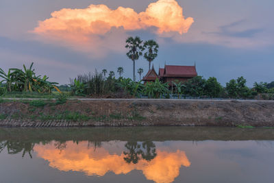 Reflection of house on lake against sky during sunset