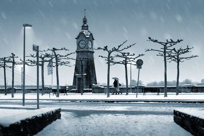 People walking on snow covered street by clock tower during winter