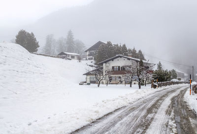 Snow covered road amidst houses and trees during winter