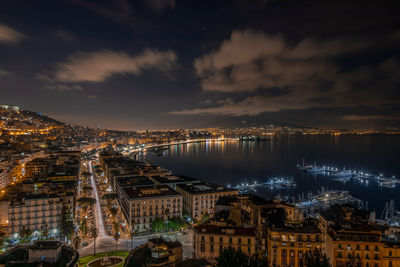 High angle view of illuminated buildings by river against sky