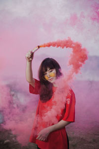 Portrait of woman holding red distress flare while standing on field