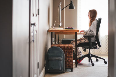 Side view of girl using computer while sitting on chair