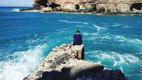 Man sitting on cliff by sea