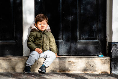 Portrait of cute boy sitting by closed house door