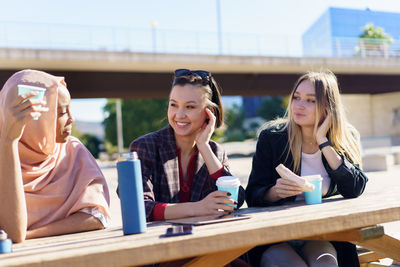 Portrait of smiling friends using mobile phone while sitting in cafe