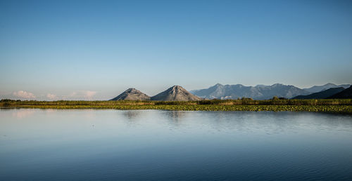 Scenic view of lake skadar by mountains against clear blue sky