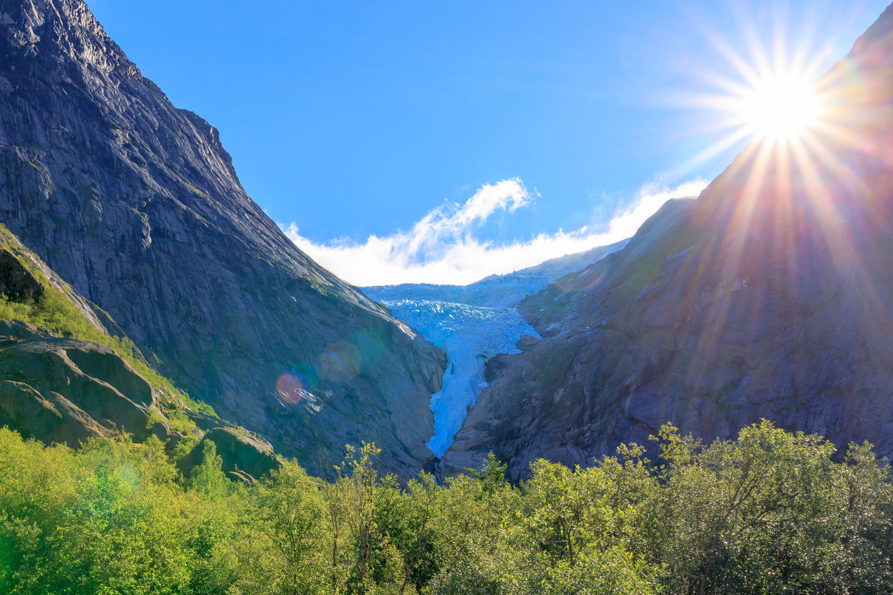 mountain, scenics - nature, sky, beauty in nature, environment, landscape, nature, mountain range, sunlight, plant, land, sun, tree, sunbeam, lens flare, tranquility, tranquil scene, forest, blue, no people, travel, pine tree, coniferous tree, travel destinations, mountain peak, snow, non-urban scene, valley, sunny, idyllic, pinaceae, cold temperature, outdoors, day, pine woodland, green, bright, wilderness, cloud, winter, summer, meadow, tourism, grass, clear sky, snowcapped mountain, brightly lit, rock, environmental conservation, leisure activity, plateau