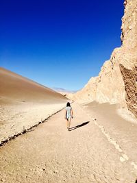 Rear view of woman walking on footpath at desert against clear blue sky