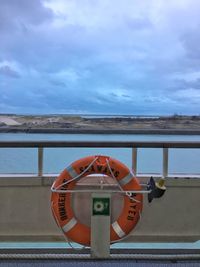 Life belt at boat deck on sea against cloudy sky