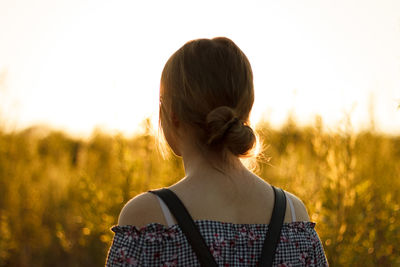 Rear view of woman standing on field during sunset