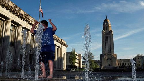 Cheerful boy standing at fountain in city against sky