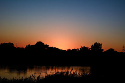 Silhouette trees by lake against sky during sunset
