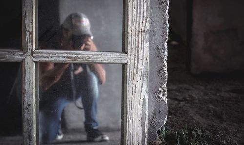 Glass window with reflection of man photographing through camera at abandoned building