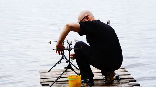 Man adjusting fishing rod on pier over lake