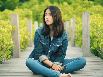 Woman looking away while sitting on boardwalk