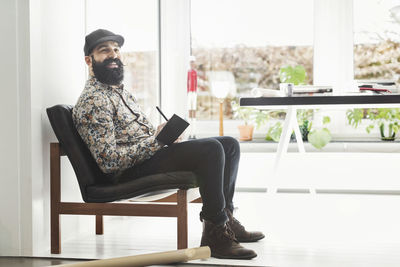 Full length of happy male architect sitting at home office