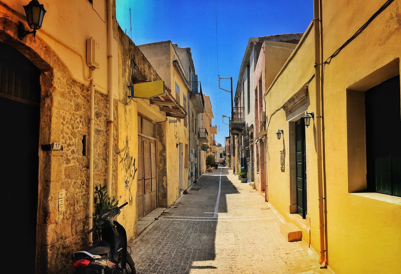 architecture, building exterior, built structure, narrow, the way forward, street, residential building, residential structure, house, shadow, long, alley, empty, diminishing perspective, walkway, clear sky, footpath, pathway, day, blue, vanishing point, outdoors, old town, residential district, no people, pedestrian walkway