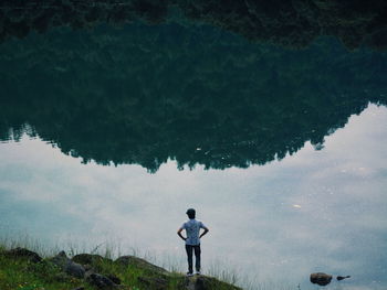 Rear view of man standing by calm lake with reflection 