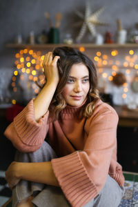 Young woman looking away sitting against christmas decoration