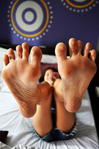 Young woman showing sole of feet while lying on bed at home