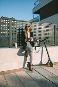 Full length of smiling businesswoman using mobile phone in city