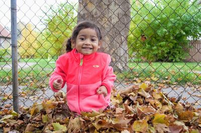 Portrait of smiling girl playing with autumn leaves against fence in park