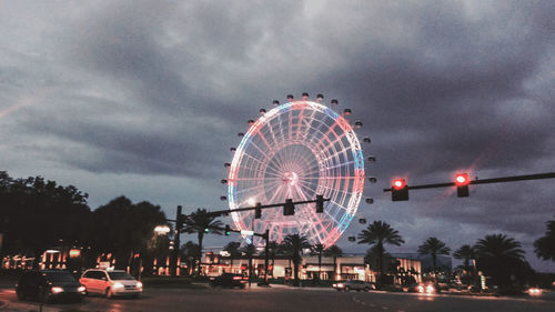 Ferris wheel by illuminated city against sky at dusk