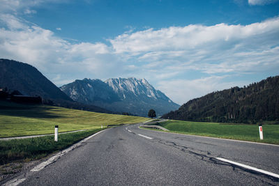 Asphalt road leading to the grip of the austrian alps. color combination of road, lawn, sky