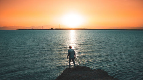 Man looking at sea against sky during sunset