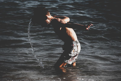 Side view of shirtless boy splashing water in sea