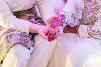 Midsection of groom putting ring in bride finger during wedding