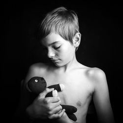 Shirtless boy with toy standing against black background