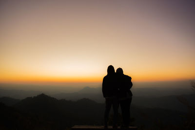 Silhouette man and woman standing on mountain against sky during sunset