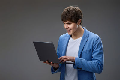 Young man using digital tablet while standing against wall