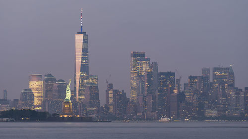 Illuminated buildings by sea against sky in city