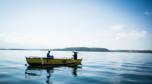 Men on boat over lake against sky