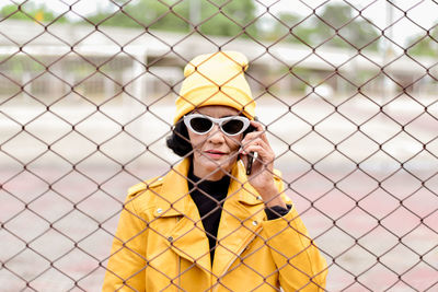 Portrait of woman talking on phone while standing by chainlnk fence