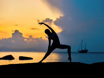 Silhouette of a young woman doing yoga exercises on the rock by the sea at sunrise