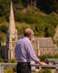 Rear view of man standing by railing against the historic church of port chalmers 