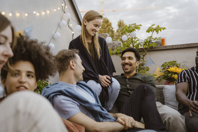 Group of male and female friends talking while sitting at party in balcony