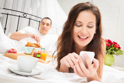 Young woman using phone while sitting on bed at home