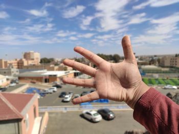 Hand of person with cityscape against sky