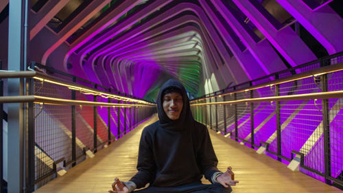 Portrait of smiling young man sitting on railing pedestrian bridge