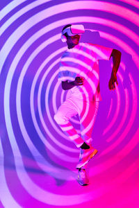 Full body stylish young african american male millennial in white t shirt experiencing virtual reality in modern vr headset in studio with colorful neon illumination