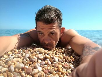 Close-up portrait of shirtless man lying at pebble beach