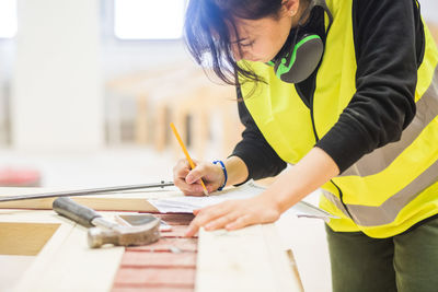 Young female trainee drawing on paper at workbench in illuminated workshop