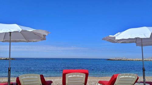 Deck chairs by sea against blue sky