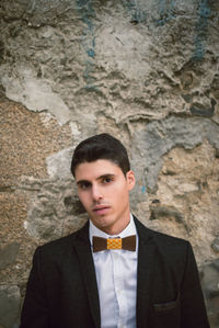 Portrait of confident young man wearing suit while standing against wall