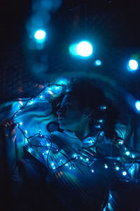 High angle view of woman holding illuminated light while lying on bed